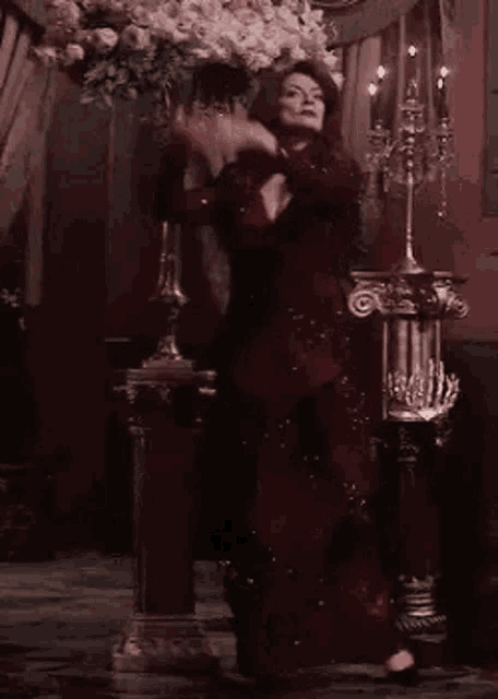 a woman in a red dress is standing in front of a vase of flowers and candles .