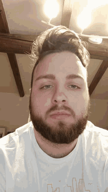 a man with a beard is wearing a white t-shirt with a cityscape on it