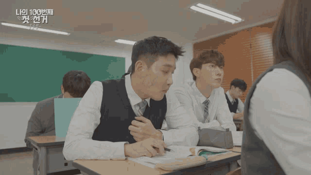 a group of students sit at desks in a classroom with a green board behind them that says ' 100 '