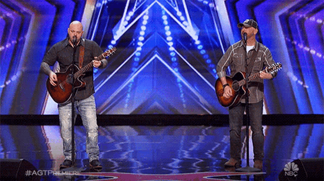 two men singing into microphones while playing guitars on a stage with the nbc logo in the background