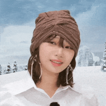 a woman wearing a brown hat and earrings smiles in front of a snowy mountain