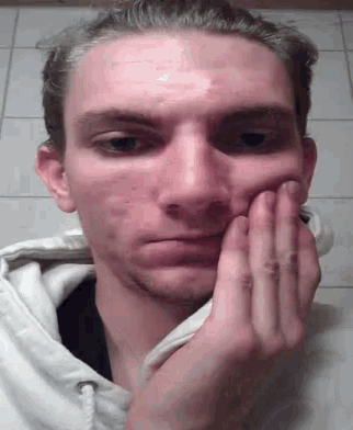 a man in a white hoodie is holding his face with his hands