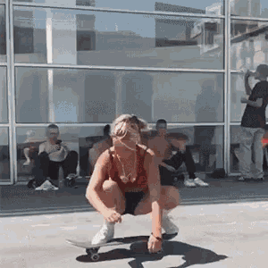 a woman is squatting on a skateboard in front of a glass building