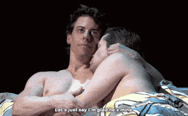 two men are laying in bed and one of them is kissing the other on the forehead .