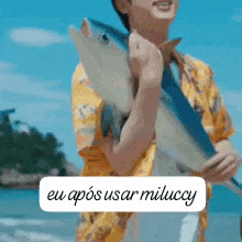 a man in a yellow shirt is holding a fish in his arms .