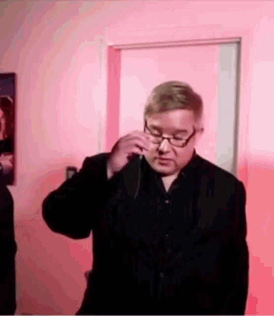 a man wearing glasses is standing in front of a pink wall
