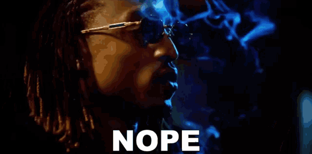 a man wearing sunglasses is smoking a cigarette and the word nope is written on the screen .