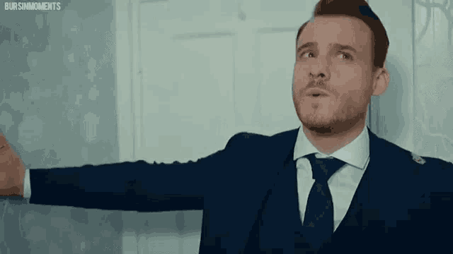a man in a suit and tie is standing in front of a door with his arm outstretched .