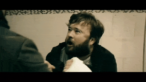 a man with a beard is holding a piece of paper in his hand while another man looks on .