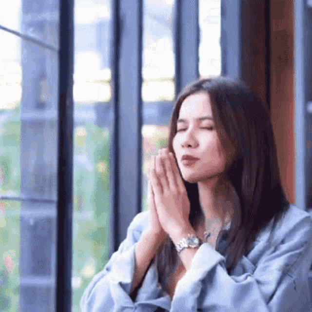 a woman is praying in front of a window with her eyes closed .