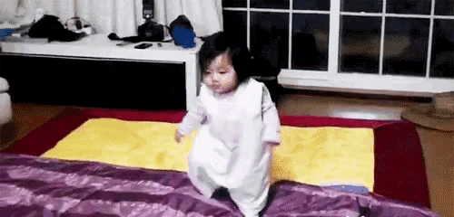 a little girl is jumping on a bed with a blanket .