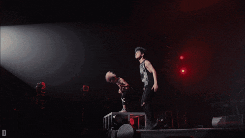 a man is jumping in the air while another man plays a guitar with the letter x on his shorts