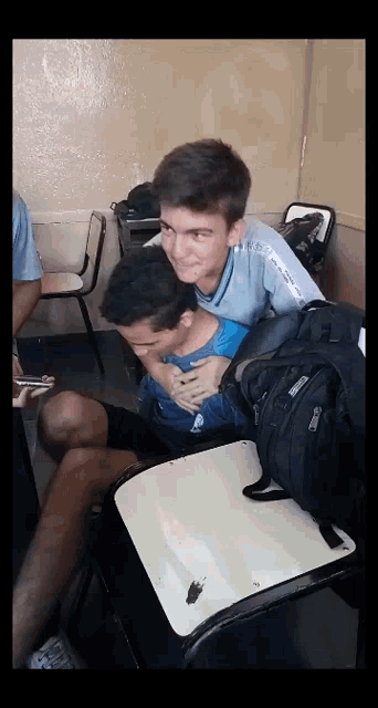 a boy in a blue shirt is hugging another boy in a white chair