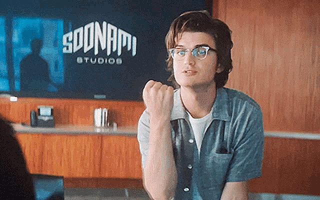 a young man wearing glasses is sitting in front of a sign for soonami studios