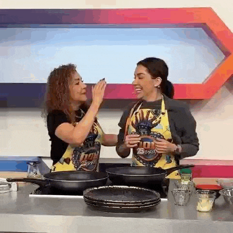 two women are standing next to each other in a kitchen holding pans .