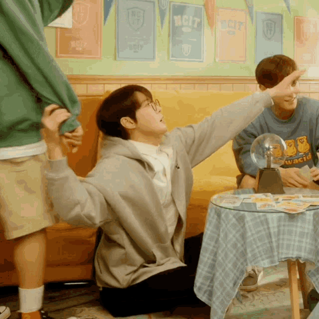 a man wearing a sweatshirt that says nct sits at a table with his arms outstretched