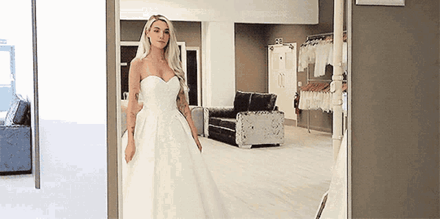 a woman in a wedding dress is standing in a room with a couch