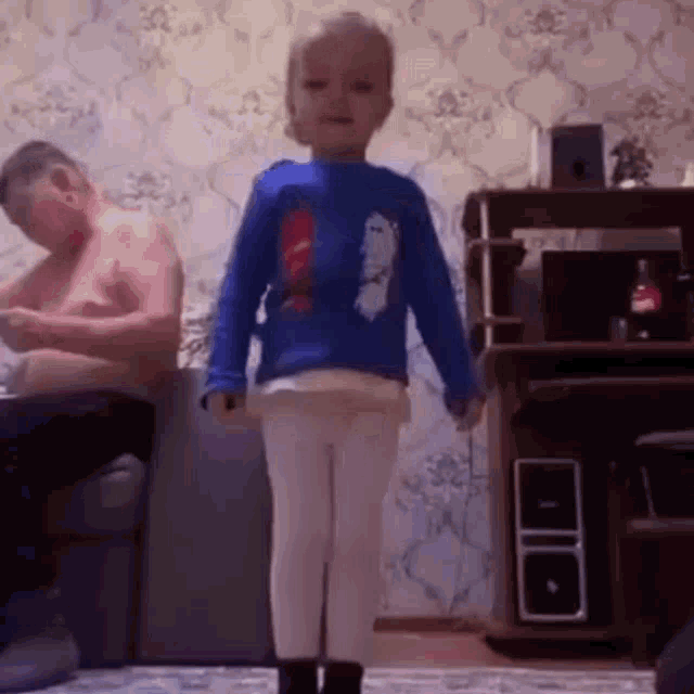 a little girl is standing in front of a man sitting on a couch .
