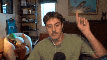 a man wearing headphones and a green shirt with the number 3 on it is pointing up