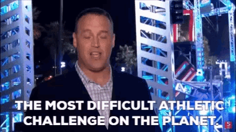 a man in a suit and plaid shirt is standing in front of a building and says " the most difficult athletic challenge on the planet "