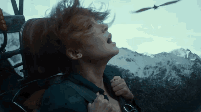 a woman with red hair is looking up at a bird flying over the mountains