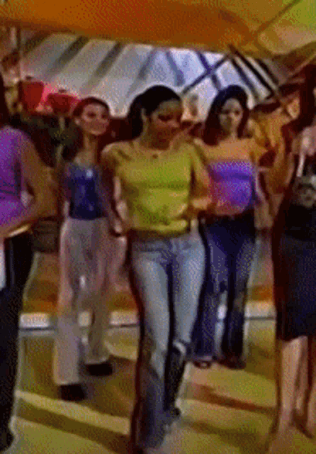 a group of women are walking in a line and one is wearing a yellow shirt
