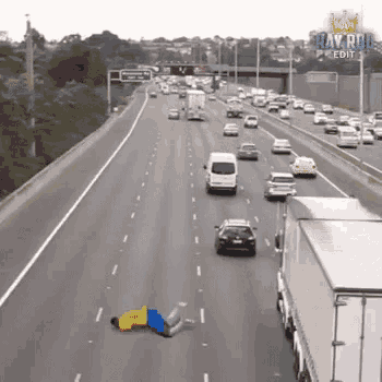 a man is laying on the side of a highway surrounded by cars and trucks .