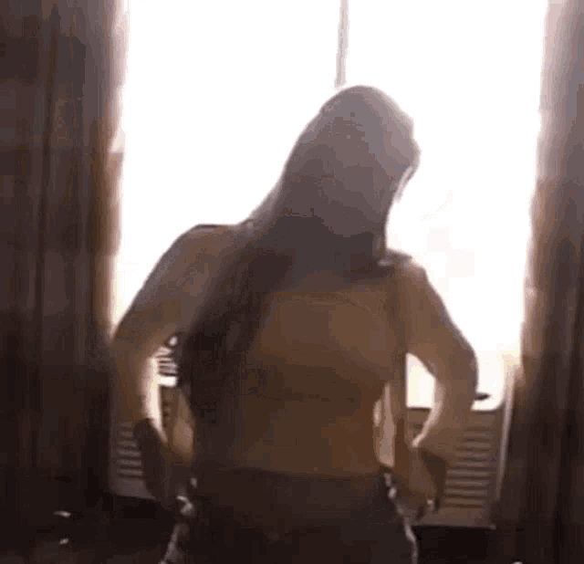 a woman is dancing in front of a window in a room without a shirt on .