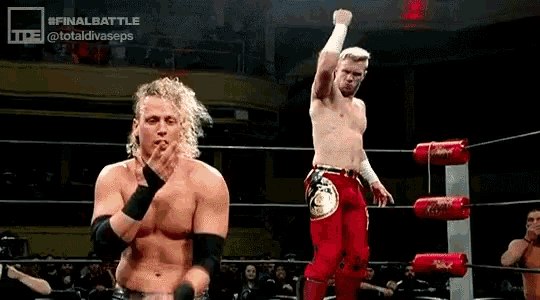a couple of men are standing in a wrestling ring . one of the men is holding his fist up in the air .