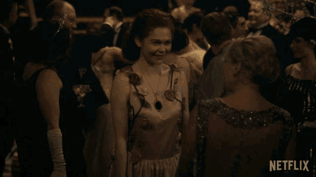 a woman in a dress stands in a crowd of people and says " thank you "