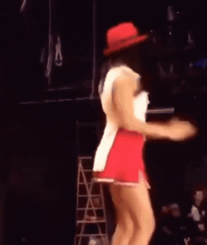 a woman wearing a red hat and a white top is dancing on a stage