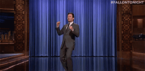 a man in a suit and tie is dancing on a stage with a blue curtain behind him .