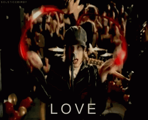 a man singing into a microphone in front of a crowd with the word love in the corner