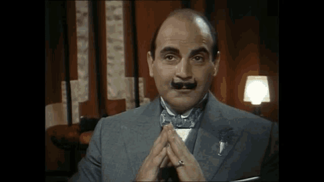 a man with a mustache and a ring on his finger is wearing a suit and bow tie