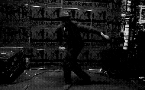a black and white photo of a man dancing on a stage in front of a wall covered in graffiti .