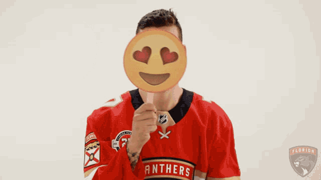 a man in a panthers jersey holds up an emoji with hearts in his eyes