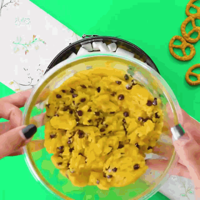 a person is holding a bowl of food with pretzels on the table