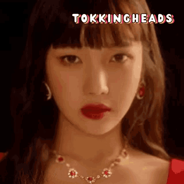 a close up of a woman 's face wearing a red dress and a gold necklace .