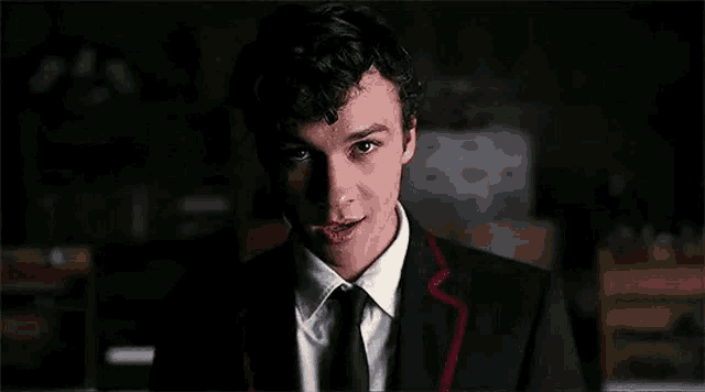 a young man in a suit and tie is looking at the camera and smiling .