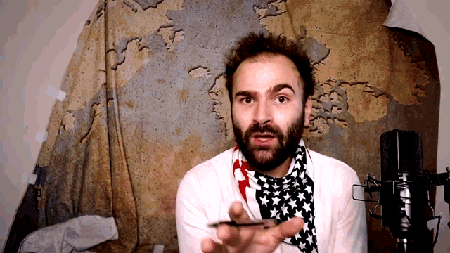 a man with a beard is standing in front of a microphone in front of a map of the world