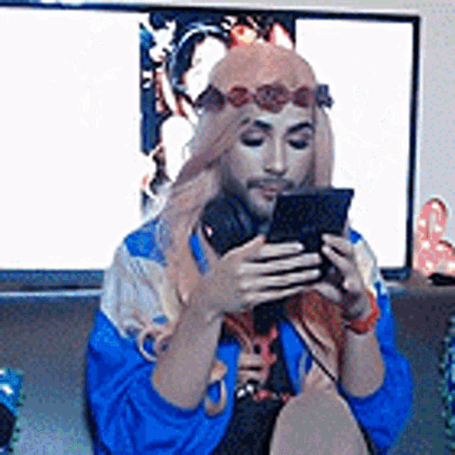 a man with a flower crown on his head is sitting on a couch looking at his phone .