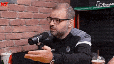 a man wearing glasses is talking into a microphone while sitting at a table .