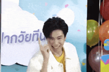 a young man is standing in front of balloons and giving a thumbs up .