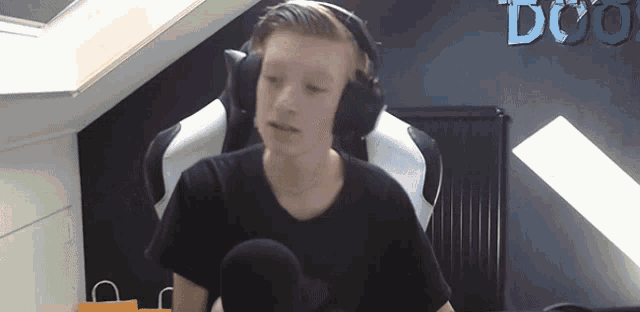 a boy wearing headphones and a black shirt is sitting in front of a wall that says doo