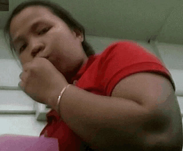 a woman in a red shirt is covering her mouth with her hands