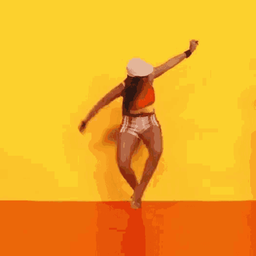 a woman is dancing in front of a yellow wall and orange floor .