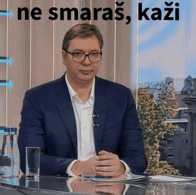a man in a suit and glasses sits at a table with the words ne smaras kazi written above him