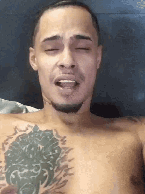 a shirtless man with a tattoo on his chest is making a funny face with his eyes closed .