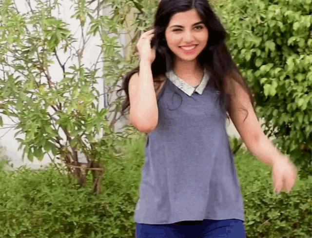 a woman in a blue tank top is smiling in front of trees