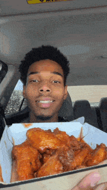 a man in a car is holding a box of wings